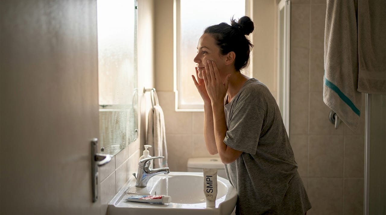 Woman applying skincare in bright home bathroom