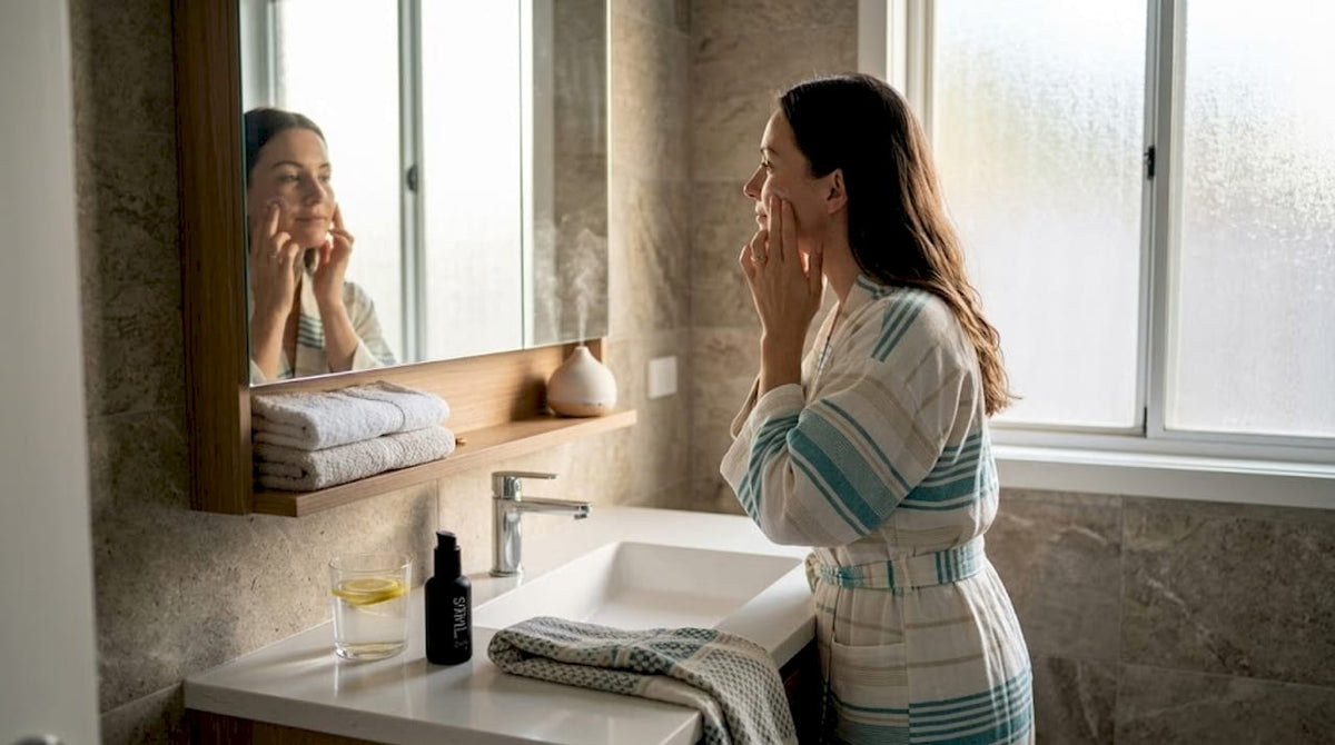 Woman moisturizing face in sunlit home bathroom